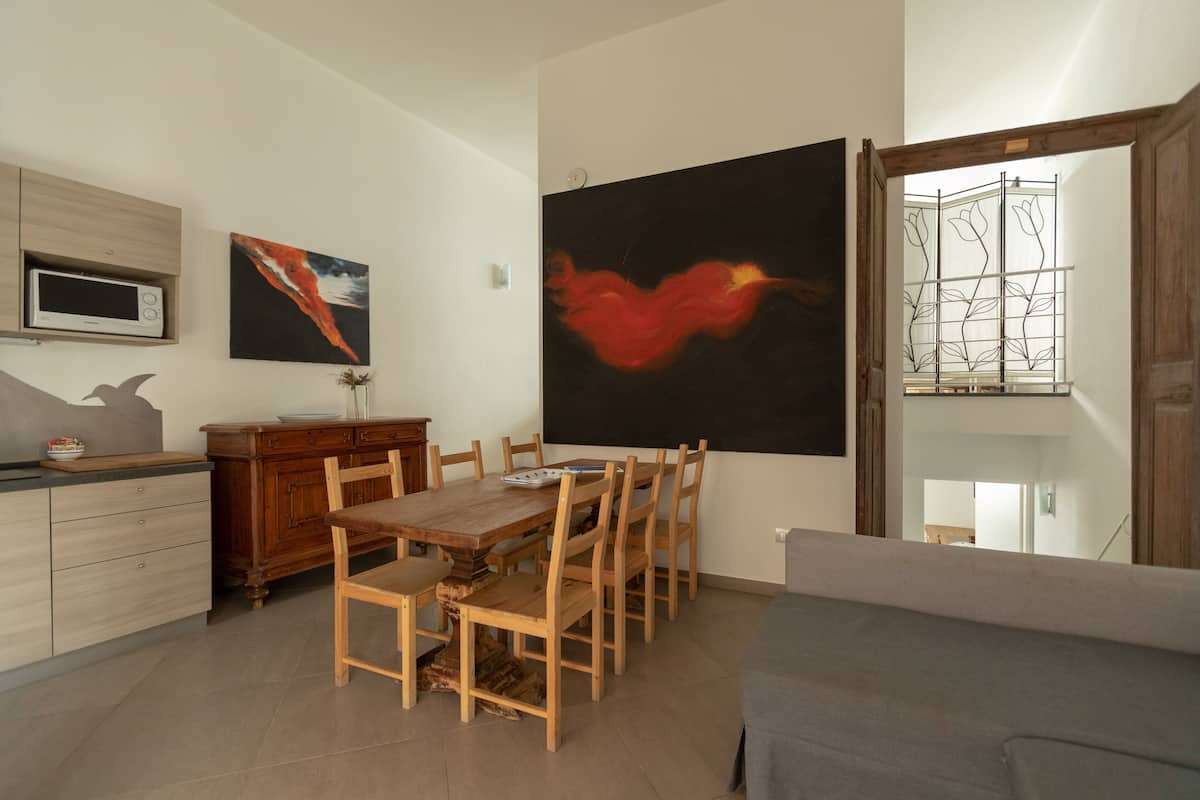 A dining area with a wooden table and chairs, a microwave, and artwork on the walls.