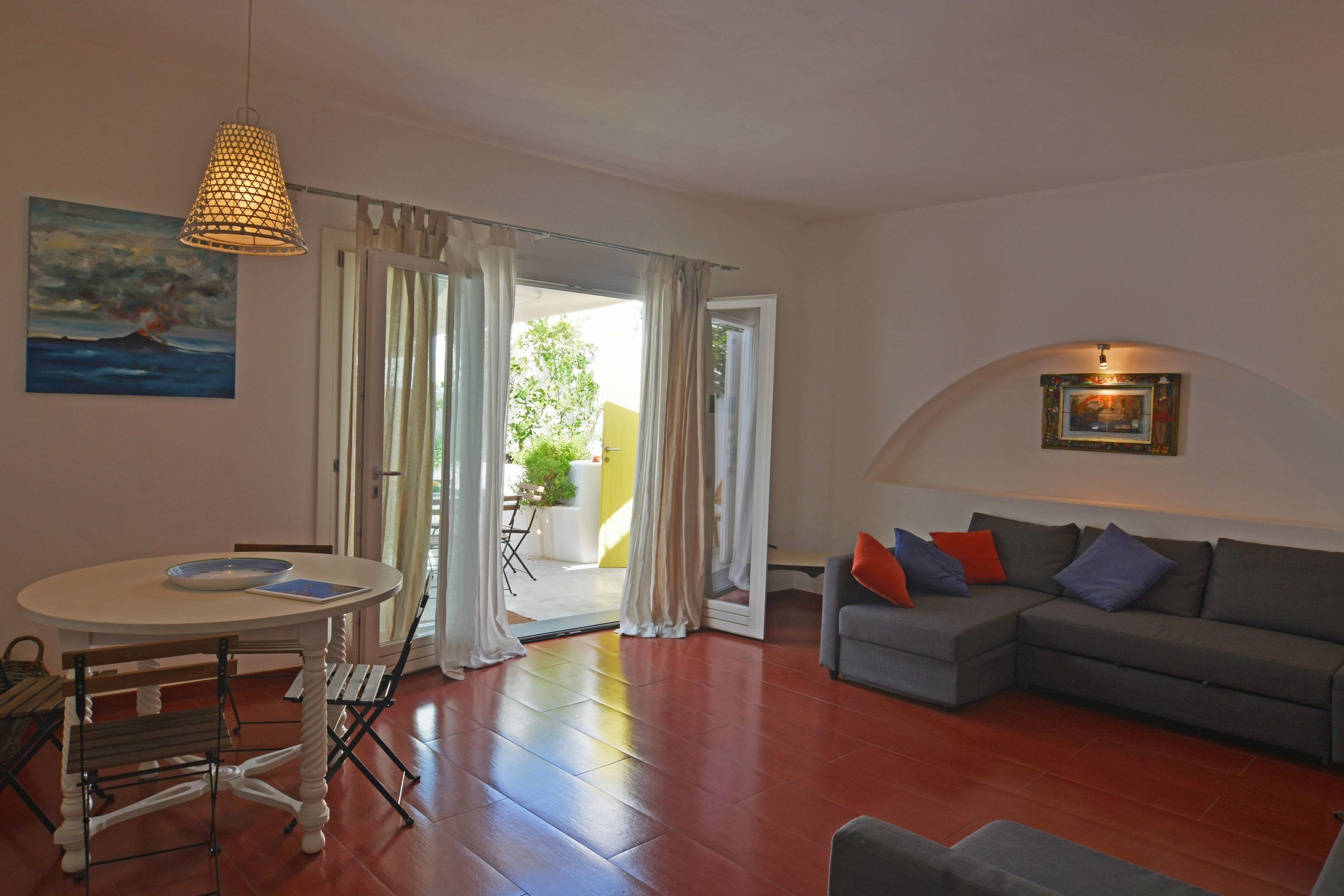 A living room with a round table, a grey sofa with cushions, and a painting on the wall.