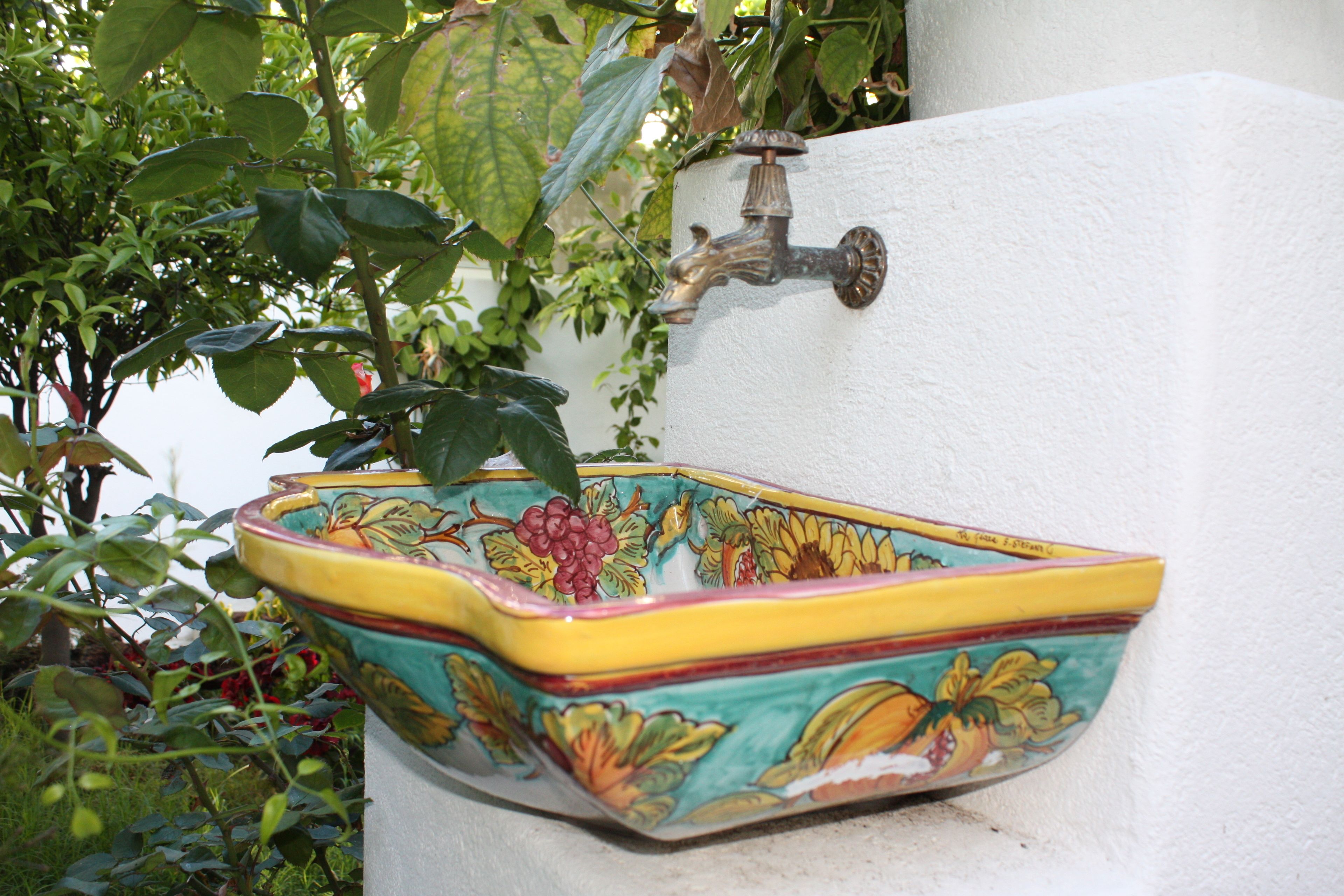 A decorative ceramic sink with floral patterns, mounted on a white wall.