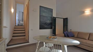 A modern living room with a white sofa, a dining table with chairs, and a staircase leading to another room.