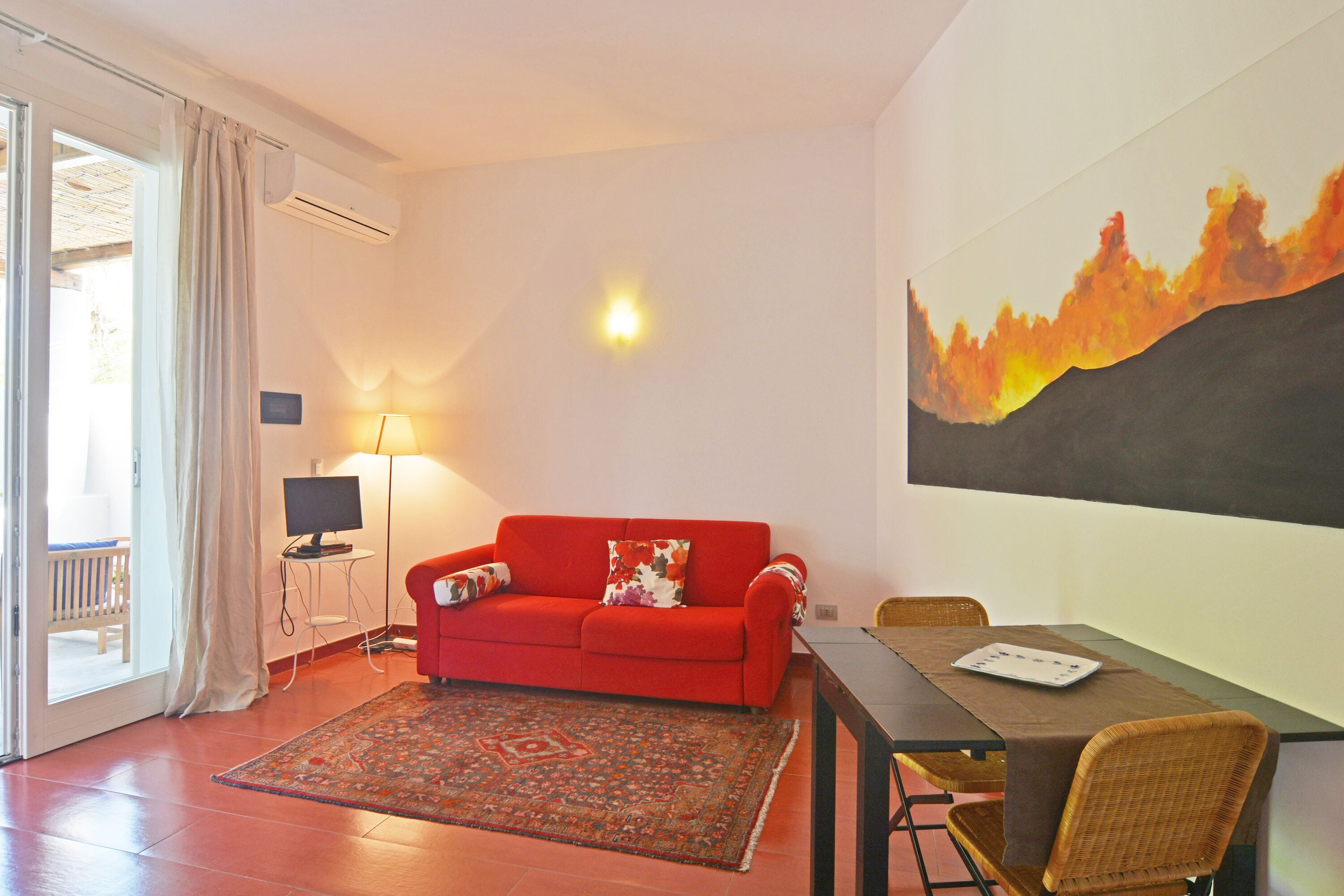 Ein Wohnzimmer mit einem roten Sofa, einem Esstisch, einem Fernseher und einem Bild an der Wand.