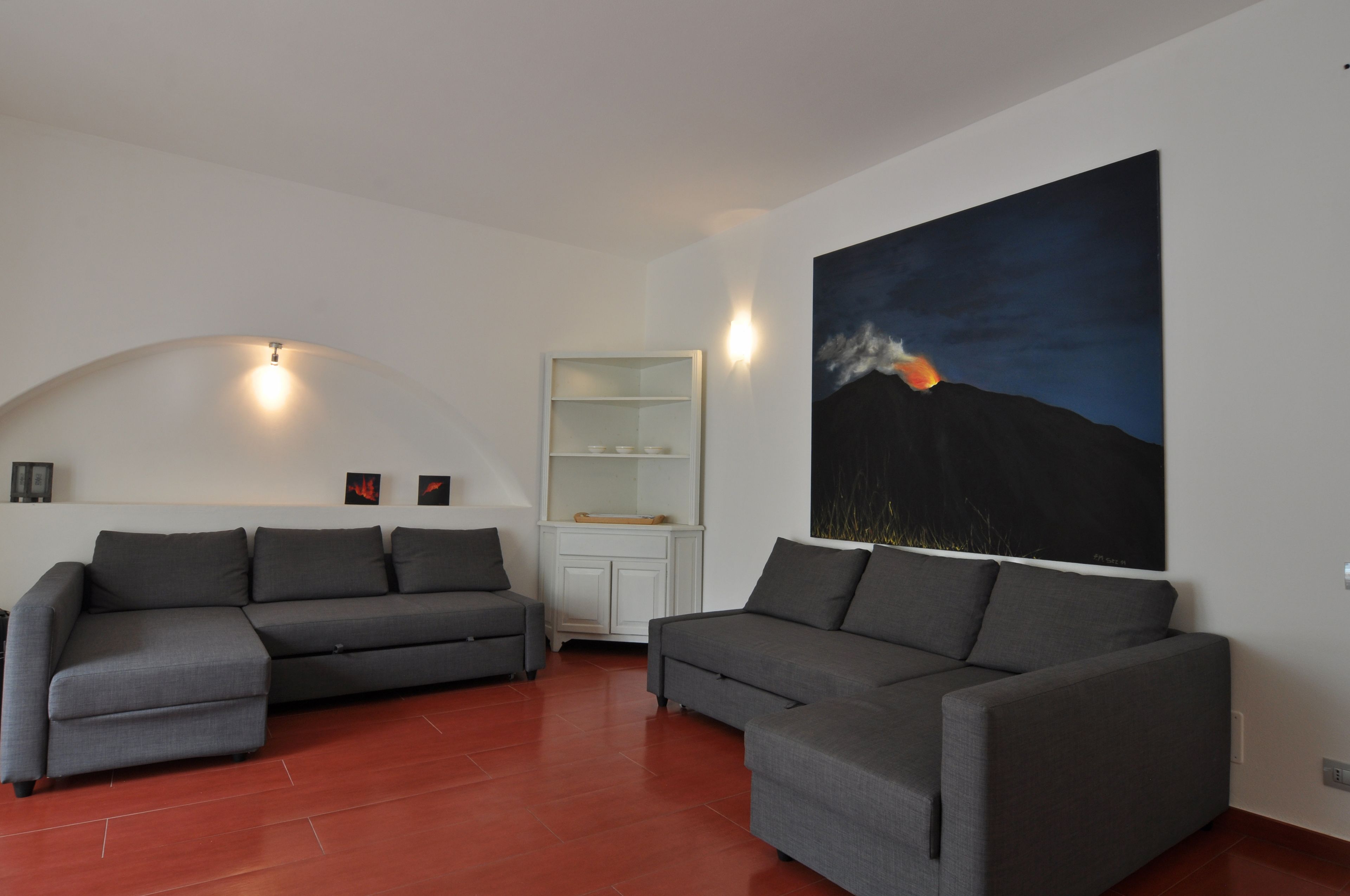 A modern living room with two grey sofas, a white cabinet, and a large painting of a mountain at dusk.