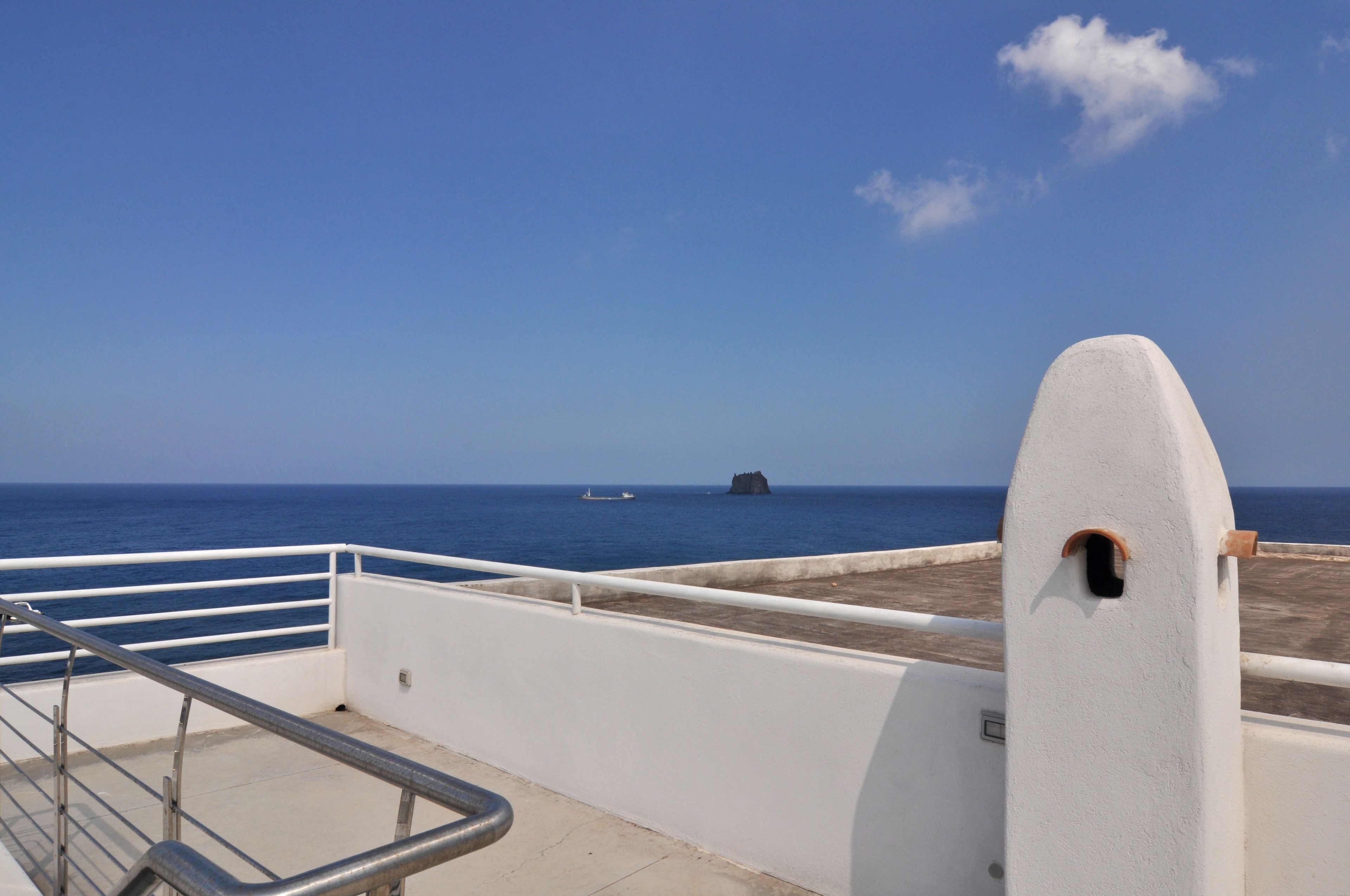 A balcony with a metal railing overlooking a clear blue sea.