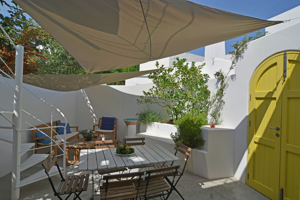 An outdoor patio with a wooden table and chairs, a yellow door, and a white wall.