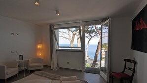 A modern hotel room with a large bed, a seating area with chairs, a small table, and a view of the sea through an open door. - Il Gabbiano Relais (Lipari)
