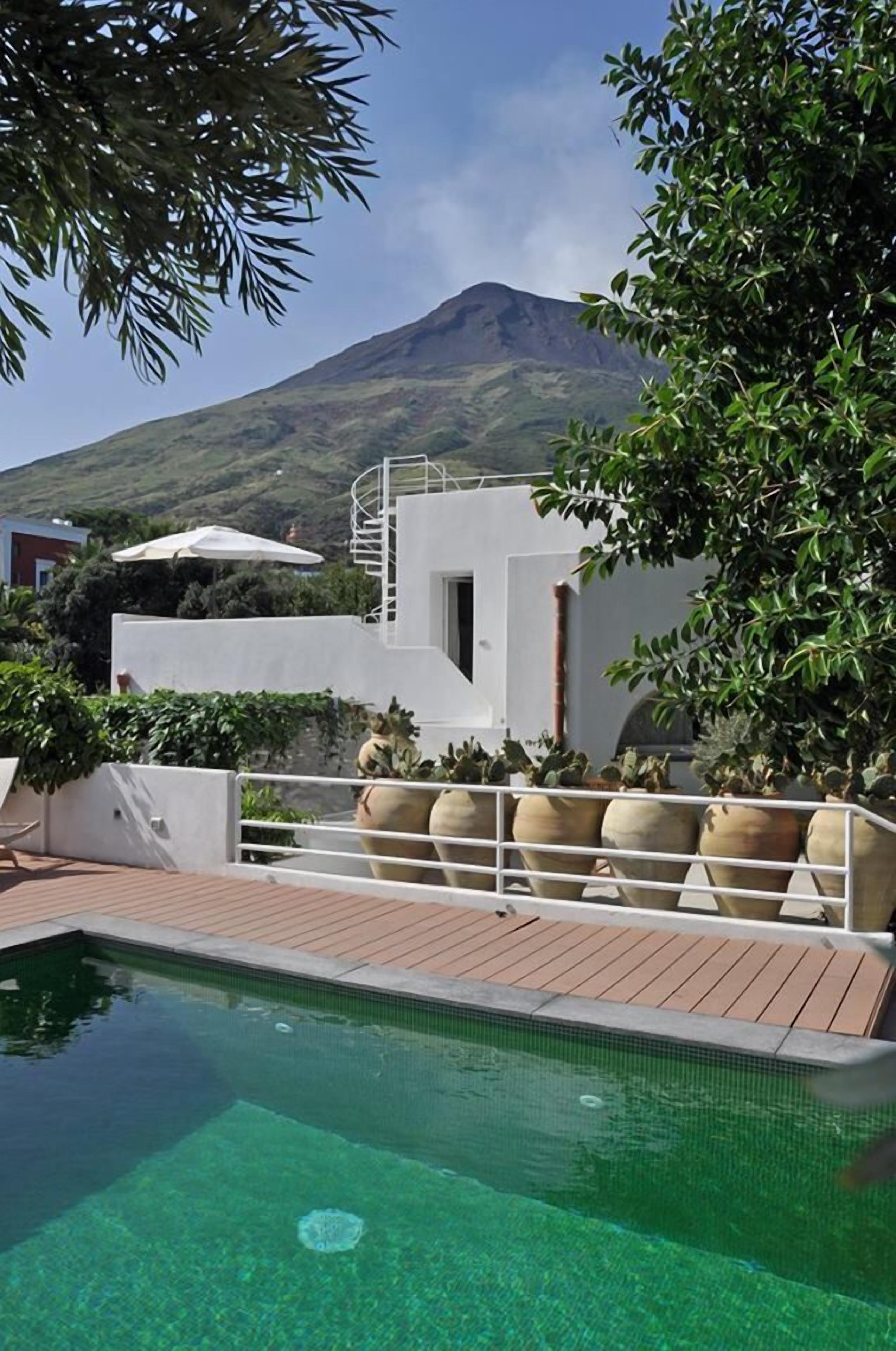 A pool area with a mountain view, a white building with a spiral staircase, and potted plants.