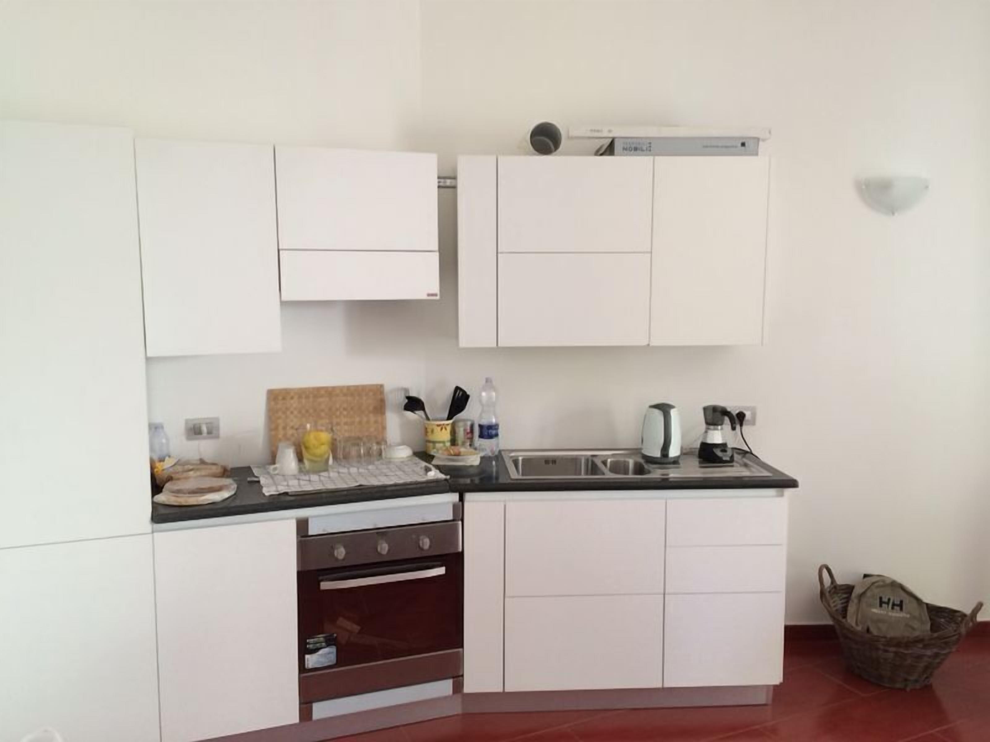 Una cocina compacta con armarios blancos, horno empotrado, lavamanos y hervidor.