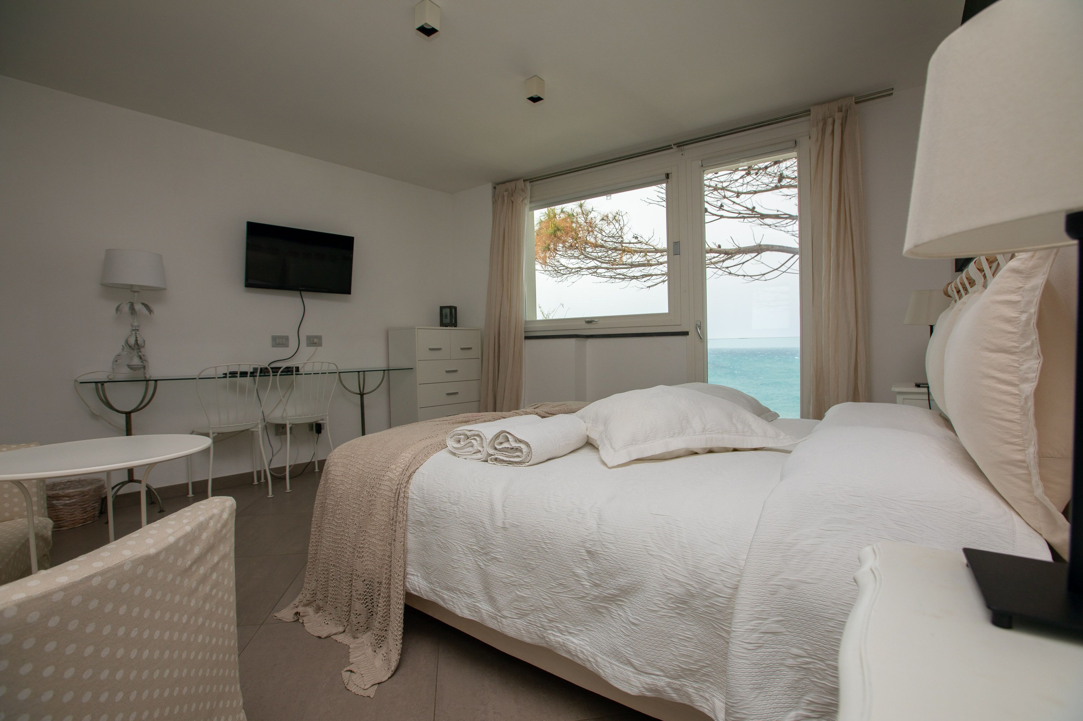 A bedroom with a bed, a TV, a desk, and a view of the sea.