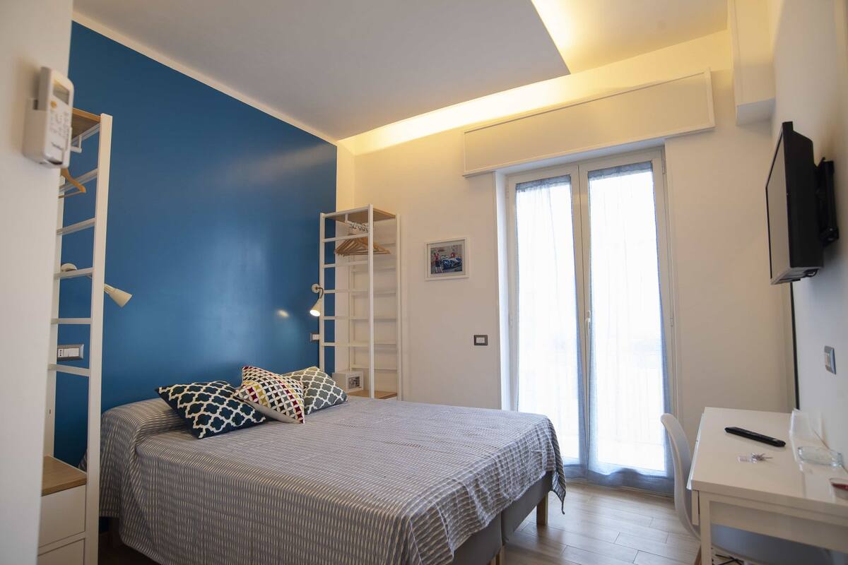 A bedroom with a bed, a desk, a chair, a wardrobe, and a window with curtains.