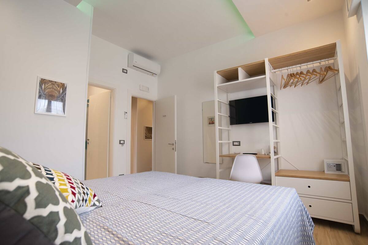 A bedroom with a bed, a wardrobe, a desk, and a TV.