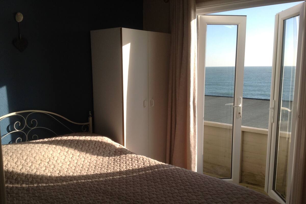 Un dormitorio con cama, armario y puerta corrediza de vidrio que da a un balcón con vistas al mar.