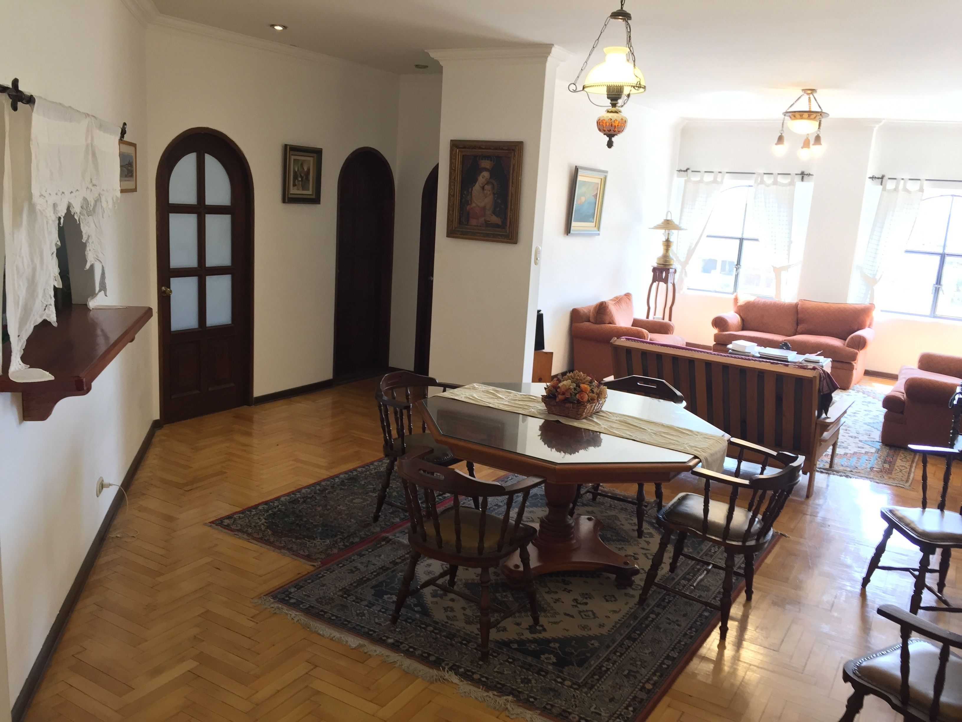 Un comedor con una mesa y sillas de madera, un tapete estampado y una araña.