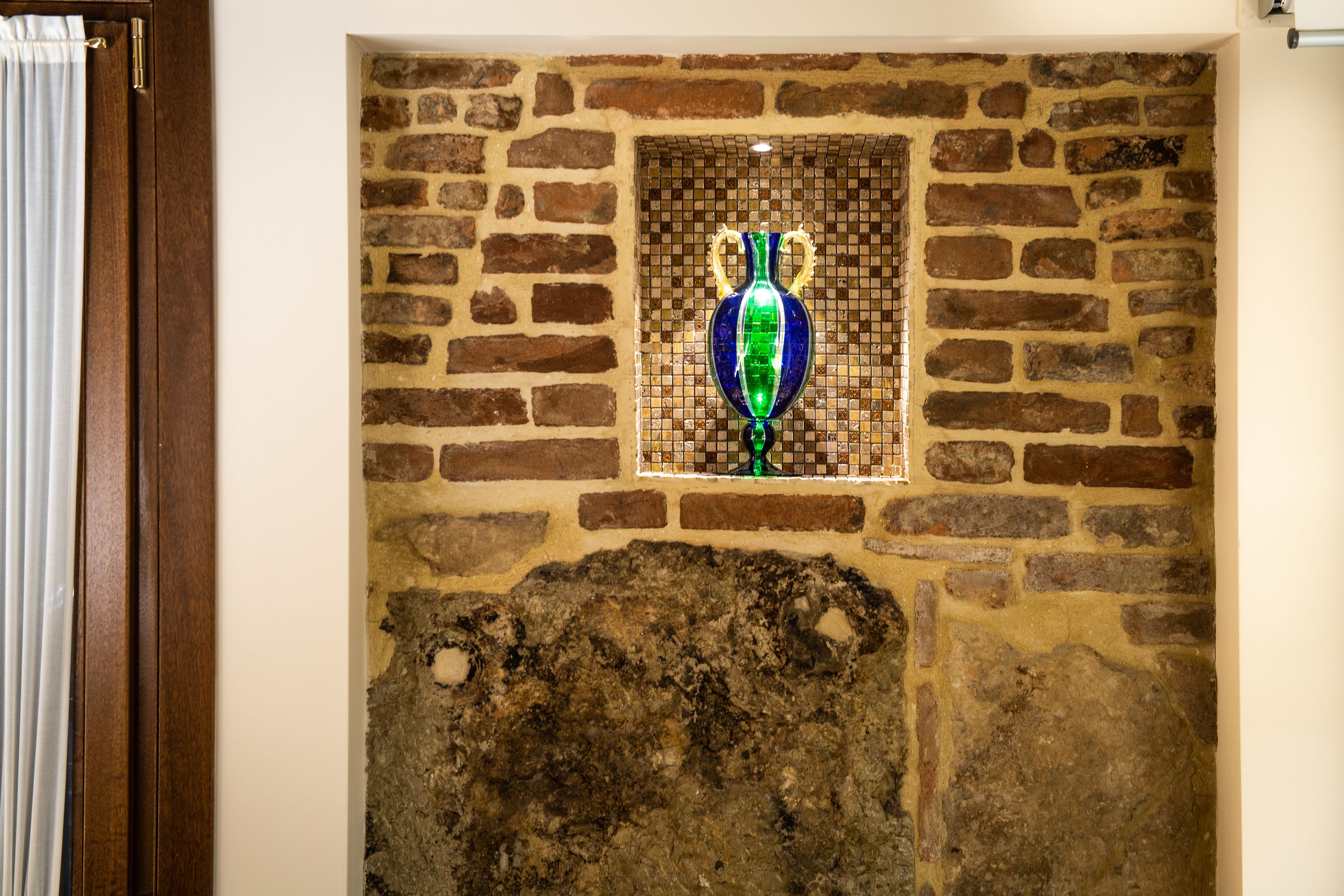 Un mur de briques agrémenté d’une fenêtre en mosaïque et d’une porte en bois.