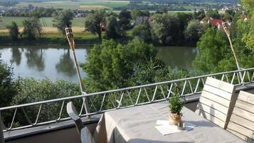 A balcony with a table and chairs overlooking a river and a village.
