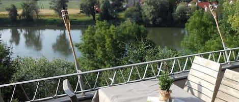 A balcony with a table and chairs overlooking a river and a village.