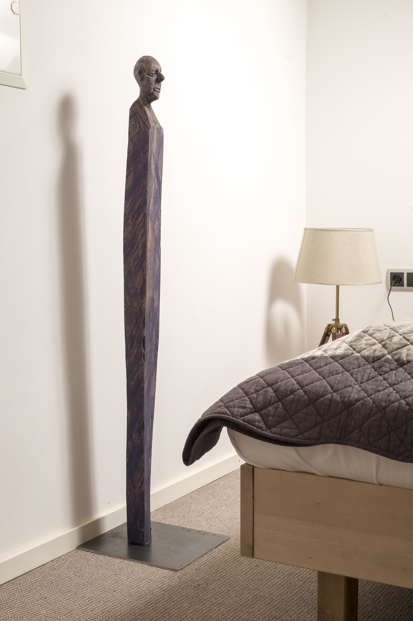 A room with a bed, a lamp, and a tall sculpture.