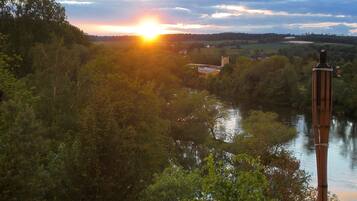 A river with a bridge, surrounded by trees and a sunset in the background.