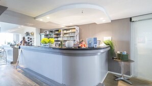 A reception area with a curved counter, shelves with various items, and a small table with a plant. - Die Aussicht (Neuburg)
