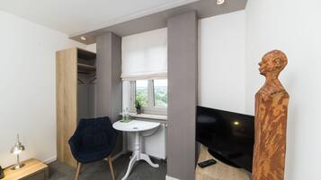 Quarto moderno com guarda-roupa de madeira, uma pequena mesa branca com cadeira, televisão e uma escultura de madeira única.