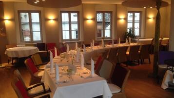 A restaurant with round tables set for dining, featuring white tablecloths and candles.