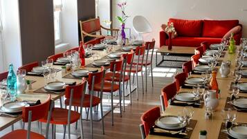 Un comedor con varias mesas dispuestas para una comida, sillas rojas y un sofá rojo al fondo.