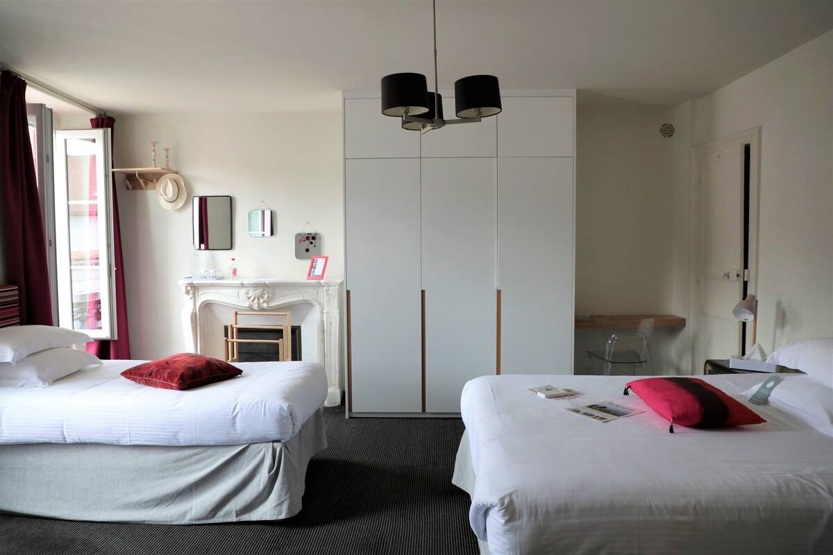 A hotel room with two beds, a fireplace, a wardrobe, and a desk with a lamp.