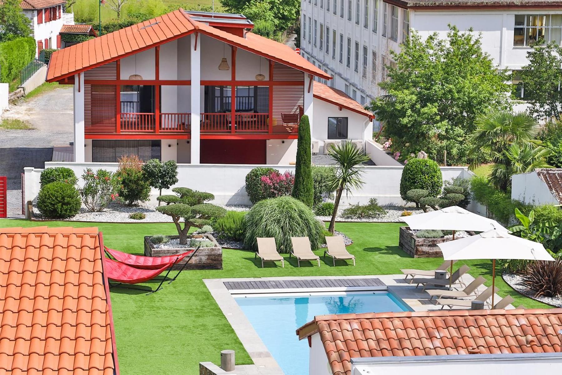 Um edifício de dois andares com telhado vermelho, piscina e área de estar externa.