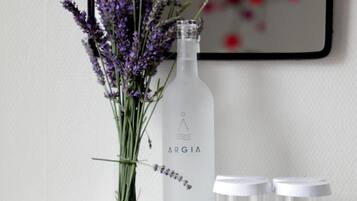 Una chimenea de mármol blanco con una botella de vidrio etiquetada 'ARGIA' y un ramo de flores de lavanda sobre una bandeja.