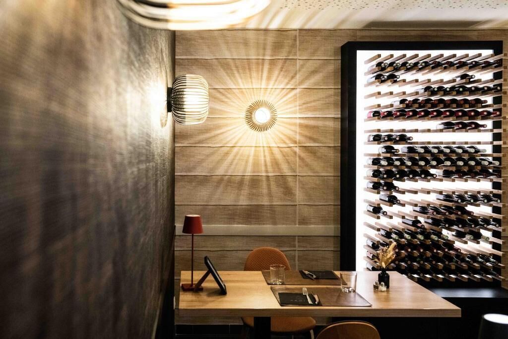 A dining area with a wall-mounted wine rack, a table with a red lamp, and a modern light fixture.