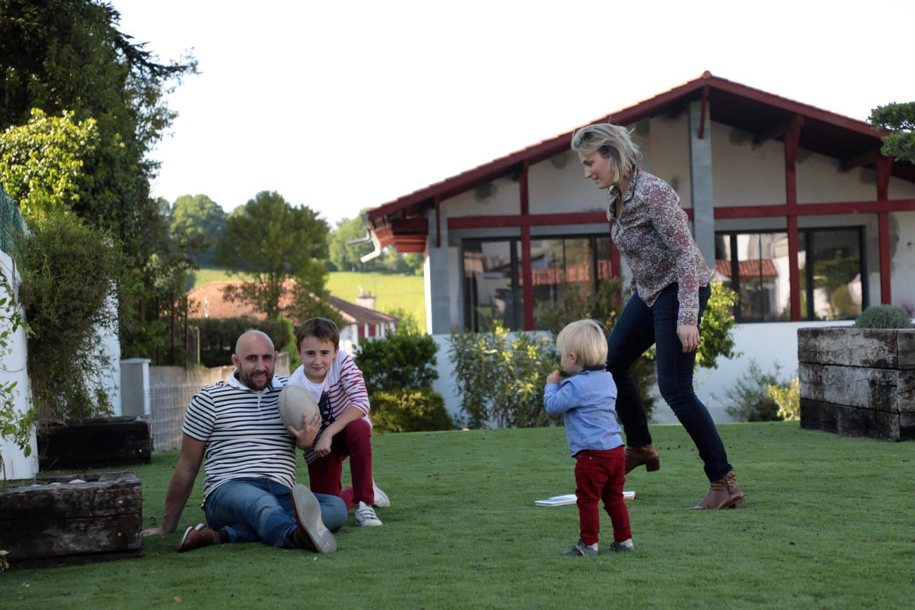 A family in a grassy outdoor area with a house in the background.