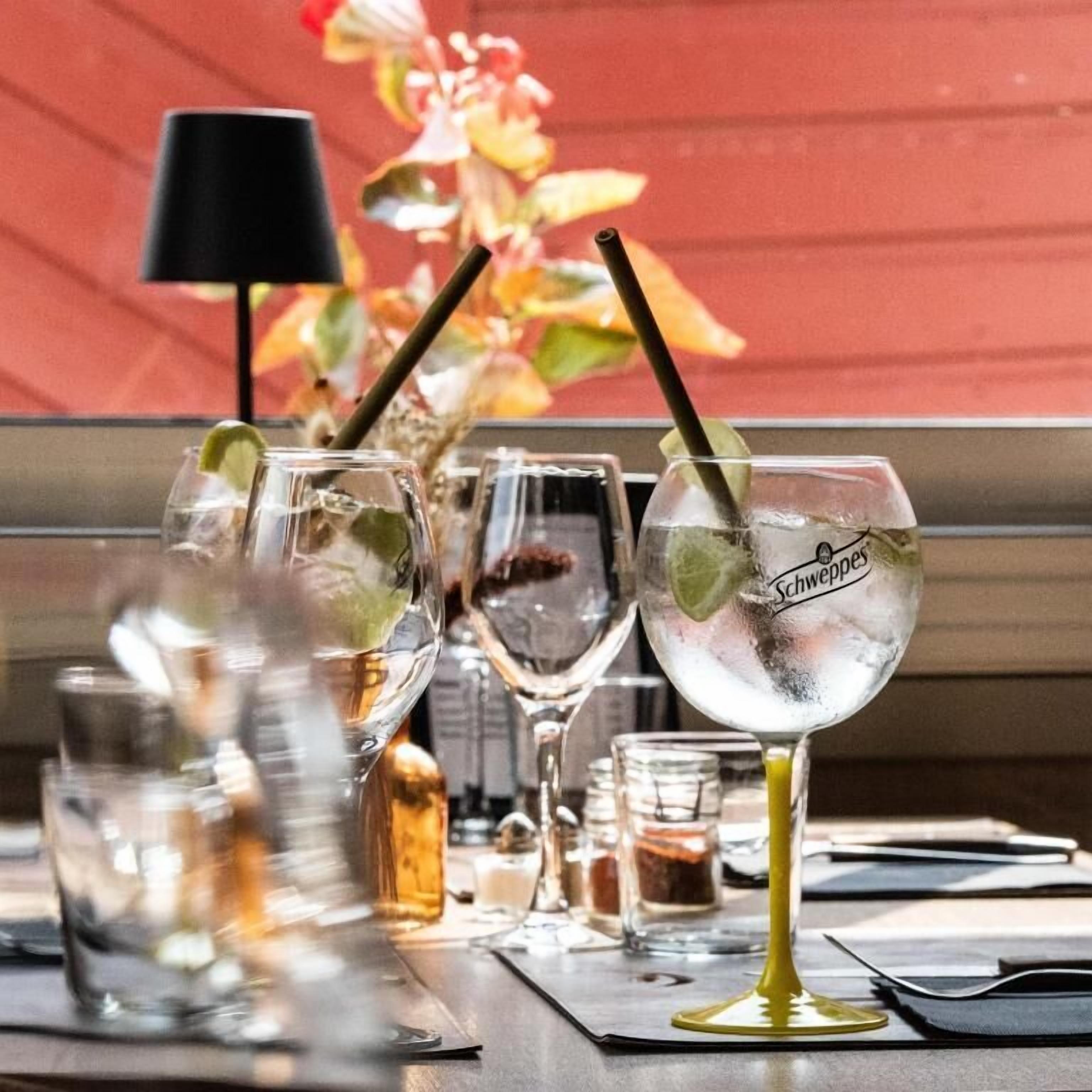 A bar area with multiple glasses of a clear beverage, some with lime and mint, and a bottle of Schweppes.