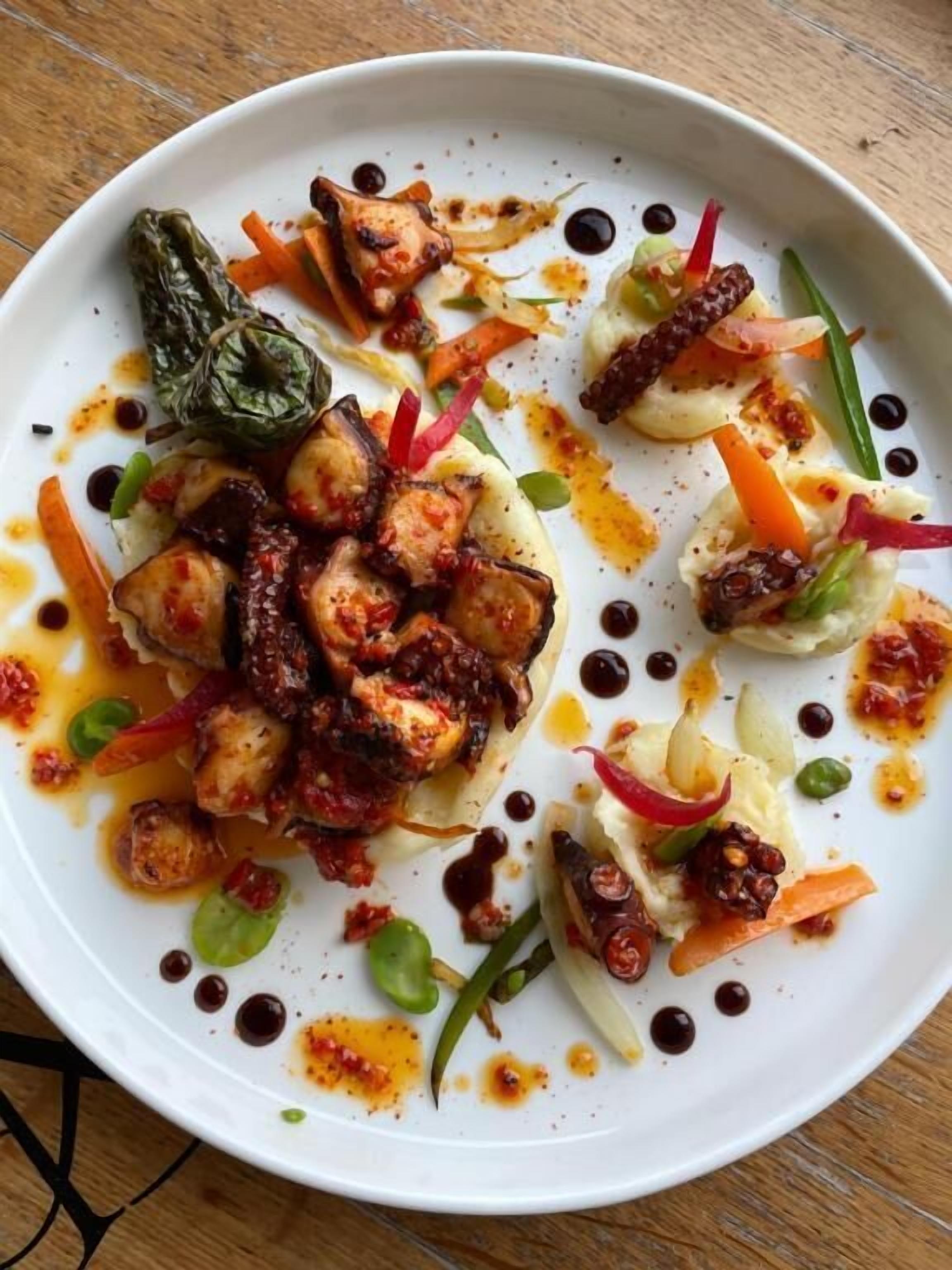 Un plato blanco con diversos alimentos, incluyendo pollo a la parrilla, verduras y una salsa.