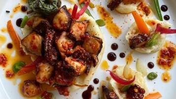 A white plate with a variety of food items including what appears to be grilled chicken, vegetables, and a sauce.
