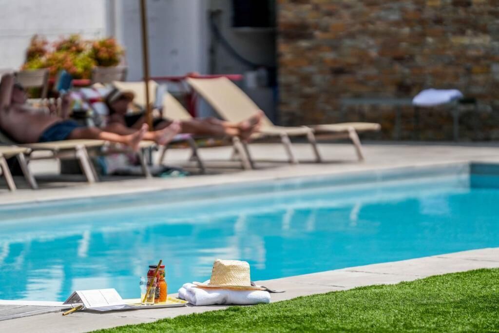 Un área junto a la piscina con sillones de descanso y una mesa pequeña con una bebida y un sombrero.