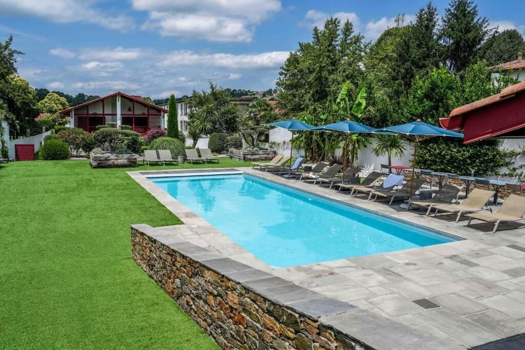 Une piscine rectangulaire bordée de pierres, entourée d’une pelouse et d’un mur en pierre.