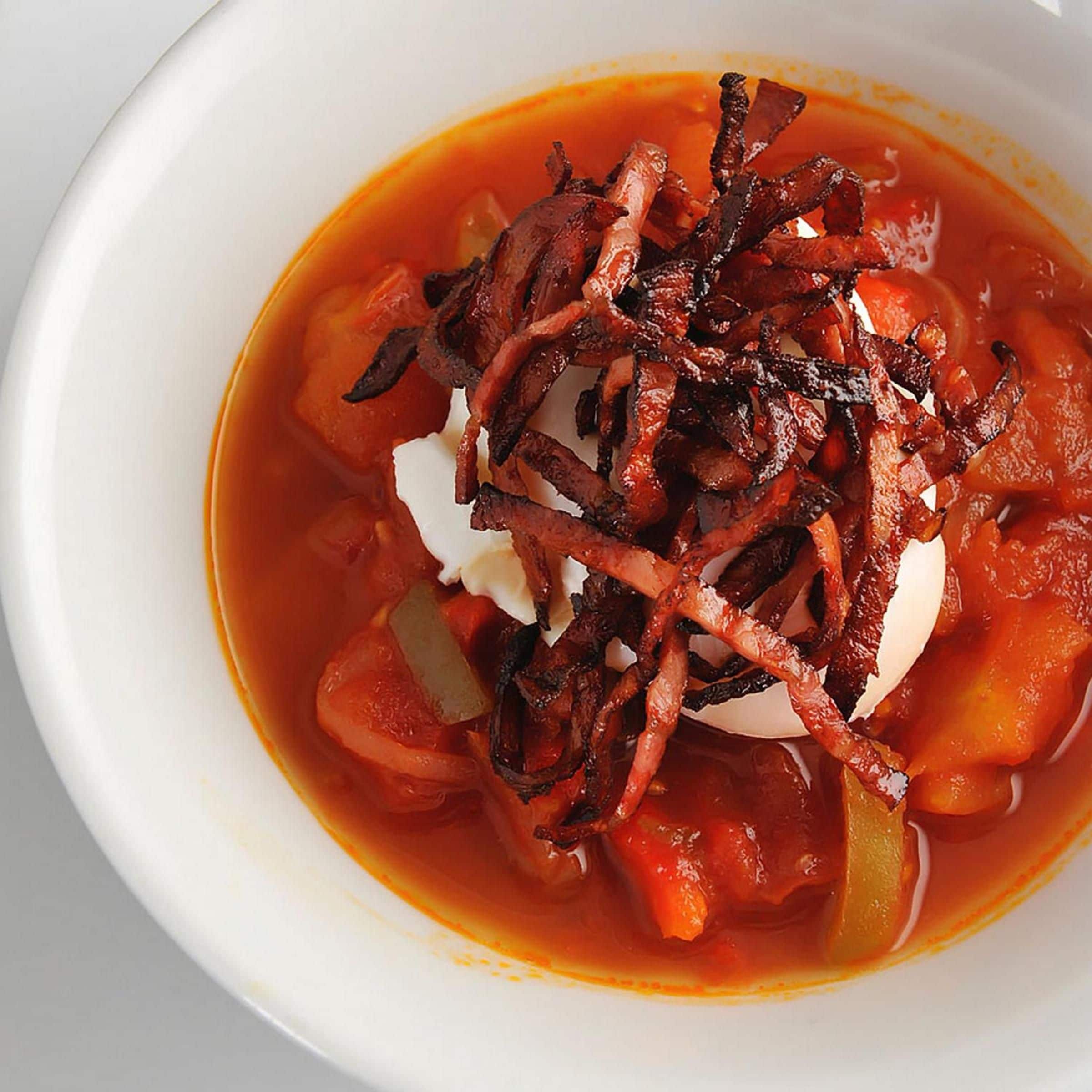 A bowl of soup with a dollop of cream and crispy bacon on top.