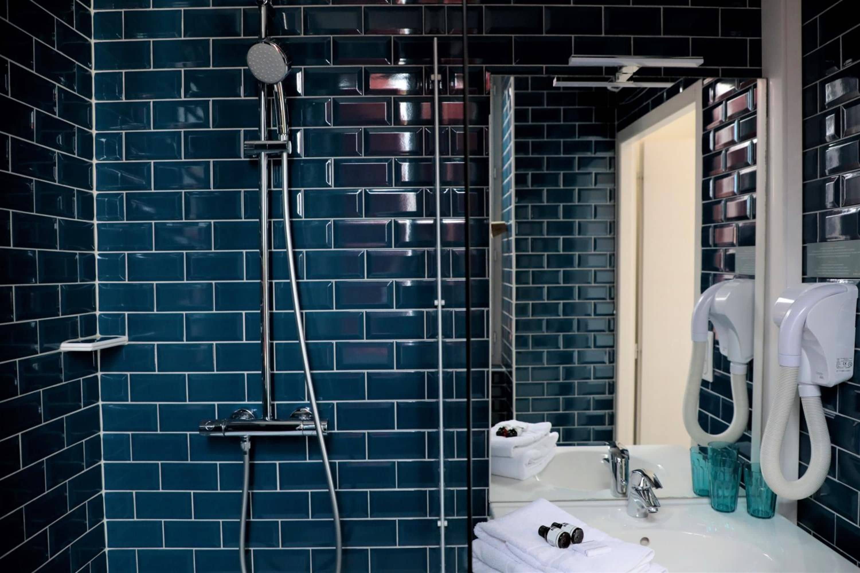 Un baño con paredes de azulejos azul oscuro, un lavamanos blanco y un cabezal de ducha de mano.