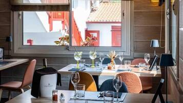 A dining area with tables set for two, a view of the outside, and a window with a view of a red building.