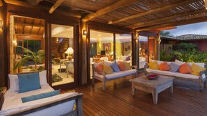 A wooden deck with outdoor seating, including a sofa and chairs, and a dining area with a table and chairs. - Txai Resort casa 10 (Itacaré)