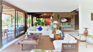 A spacious living area with a large sofa, a coffee table, and a dining table. There is a kitchen area visible in the background. - Txai Resort casa 10 (Itacaré)