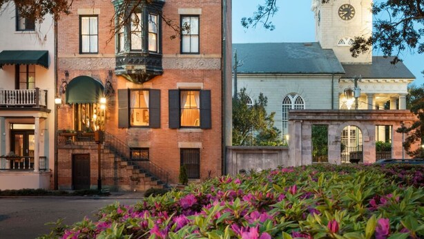 A historic building with a clock tower, a staircase leading to a balcony, and a well-maintained garden with flowering plants. - Foley House Inn (Savannah)