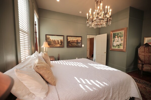 A bedroom with a large bed, a chandelier, and framed pictures on the wall.