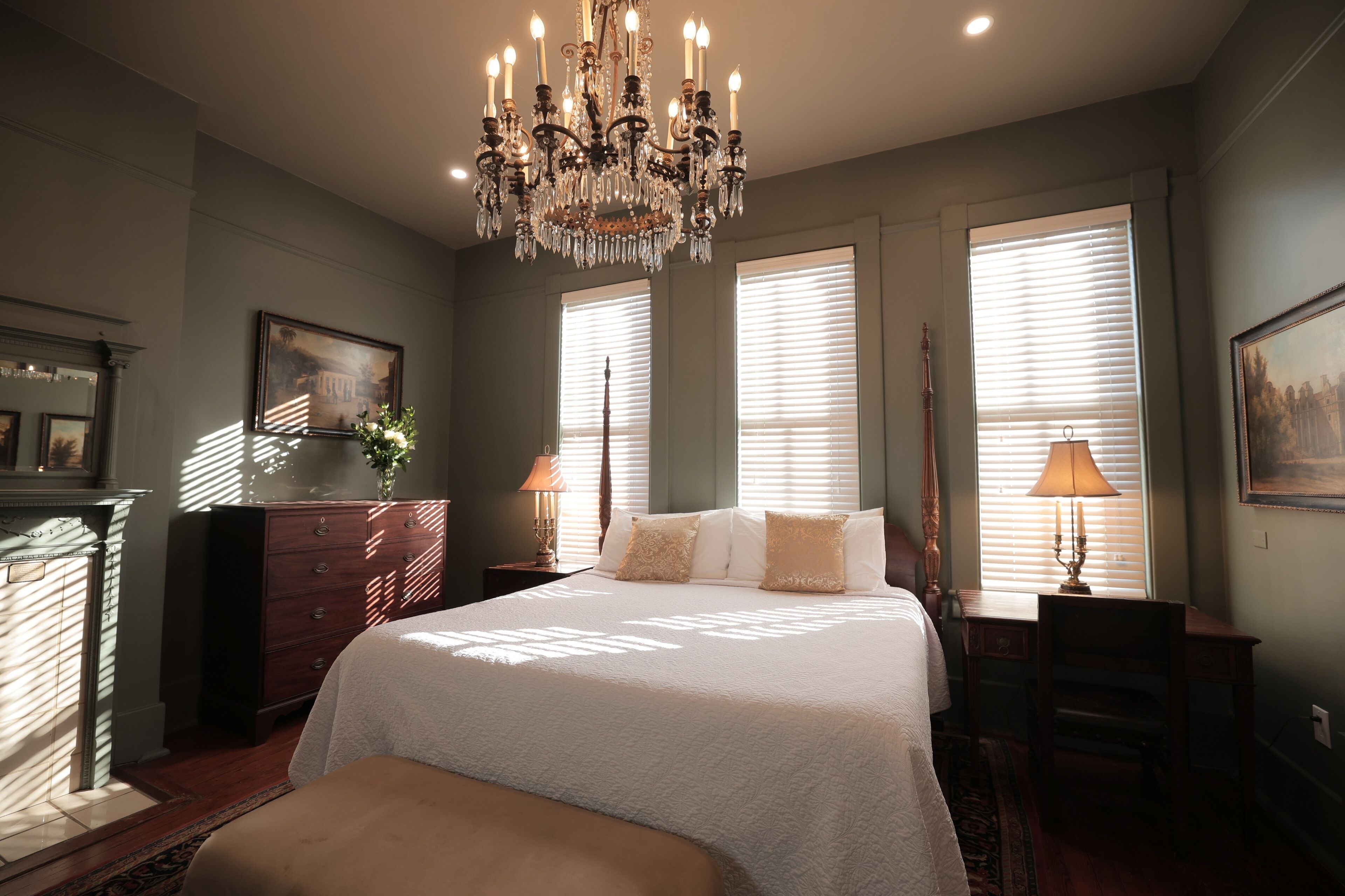 A bedroom with a large bed, a chandelier, a dresser, and a desk with a lamp.