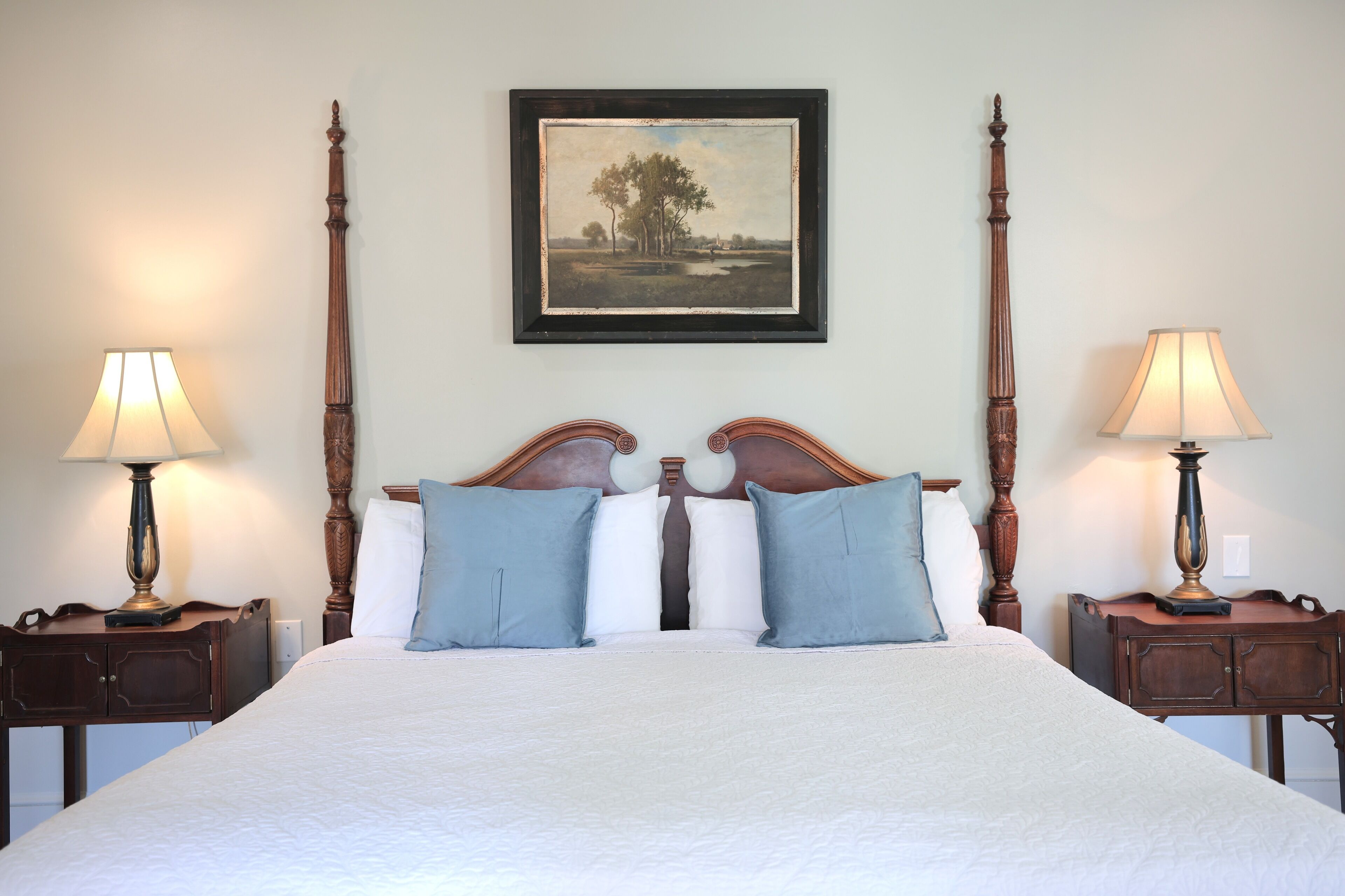 A large bed with a wooden headboard, two nightstands with lamps, and a framed landscape painting on the wall.