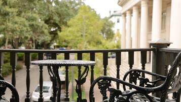 A balcony with ornate metal furniture, a view of a tree-lined street, and a building with columns in the background.