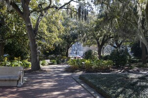 Un chemin pavé bordé d’arbres et agrémenté d’un banc, qui mène à un bâtiment.