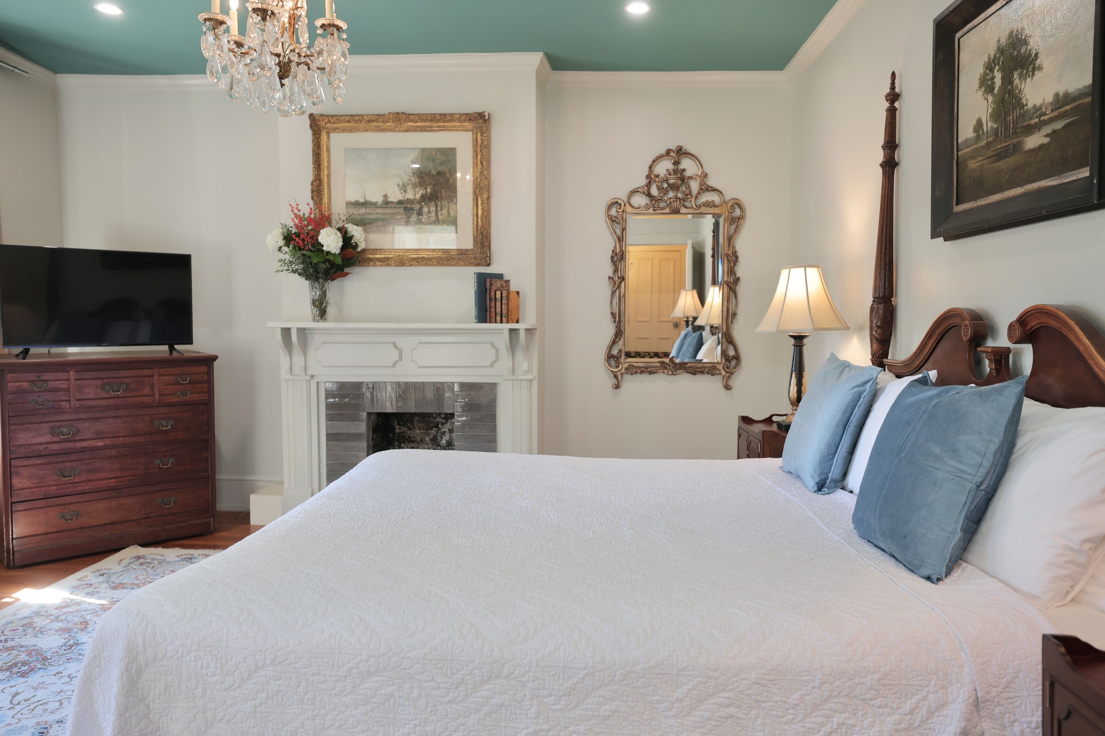 A bedroom with a large bed, a dresser, a television, a fireplace, and a chandelier.