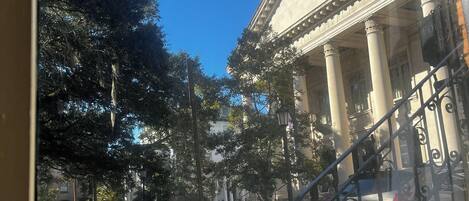 A view of a street with a building featuring classical architecture, including columns and a portico.