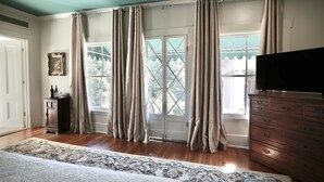 A bedroom with a large bed, a dresser, a television, and a window with curtains. - Foley House Inn (Savannah)