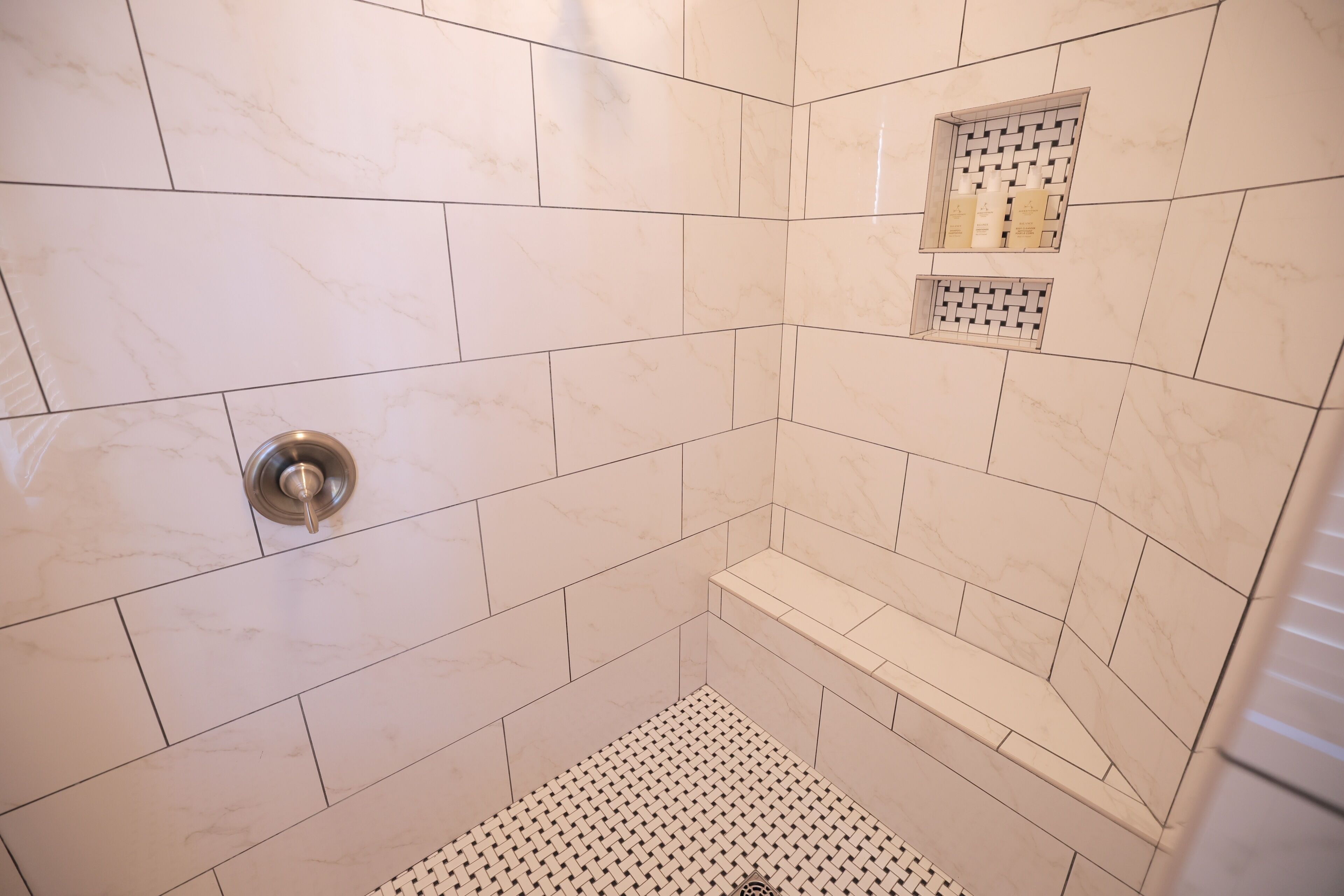 Een douche met witte tegels en een klein plankje met toiletartikelen.